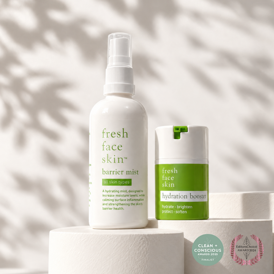Two Fresh Face Skin skincare bottles displayed on a white pedestal: a white spray bottle labeled barrier mist and a white tube with a green cap labeled hydration booster, set against a softly lit background with leaf shadows.